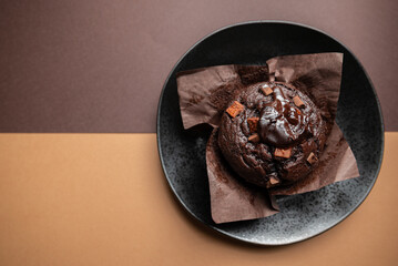 A chocolate muffin with chocolate chips on top of it. The muffin is sitting in a paper cup