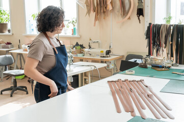Caucasian woman makes belts from genuine leather in a workshop.  - obrazy, fototapety, plakaty