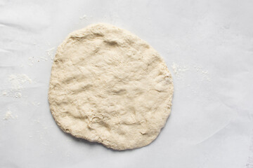 Overhead view of bread dough on parchment lined baking sheet, Shaping proofed dough on a white...