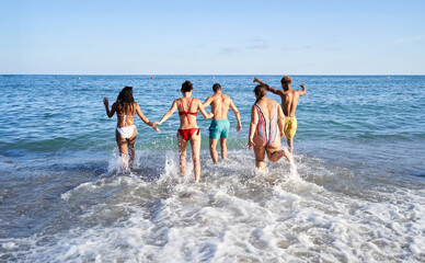 Rear view of a happy unrecognizable group of people running to get into the beach. Young friends having fun on summer holidays. Wide shot with copy space.