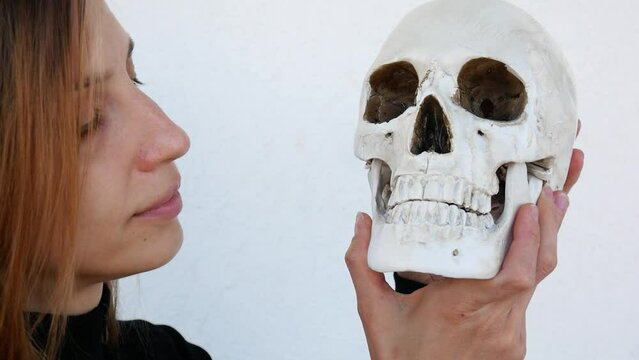 Close-up of a beautiful lady kissing a human skull on the cheek