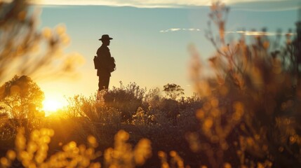 A man in a hat standing in a field at sunset. Suitable for outdoor and nature themes