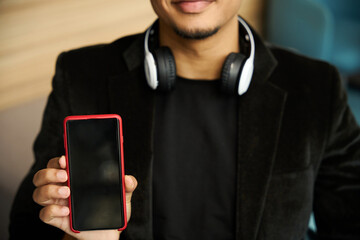 Happy guy wearing headphones on neck showing phone screen