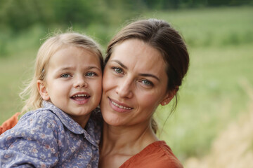 Mother and daughter hugging in countryside on blurred green background