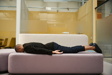 Tired male employee sleeping on sofa in office