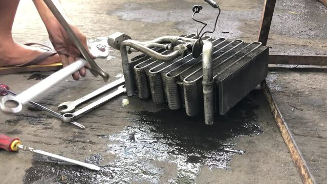 Technician is disassembling the heat exchanger evaporator component of a car on the street pavement. Close up