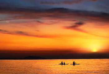 Silhouette of two people kayaking on the sea at sunset, young couple on a kayak on the sea at dusk under the light of the big moon Actively rest Swim away from problems privacy concept. - image