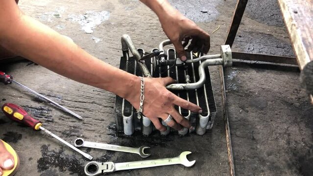 Technician is disassembling the heat exchanger evaporator component of a car on the street pavement. Close up