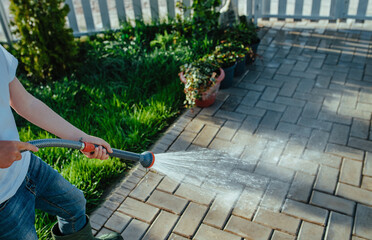 Boy cleans the walkway with water jet from a hose in summer