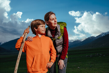 Young woman with her son standing in the mountains in twilight and looking away