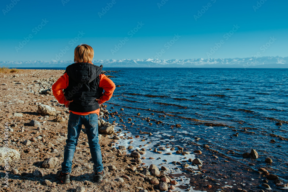 Wall mural Boy standing on the shore of the lake and admiring the scenery, back view