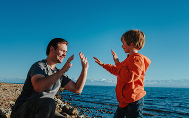 Father and son playing hands by the lake on a summer day