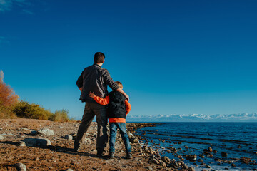 Father and son standing together on shore of the lake, back view