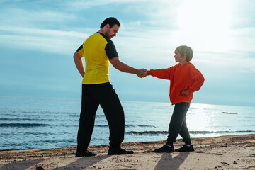 Father and son shaking hands on lake shore at sunny day