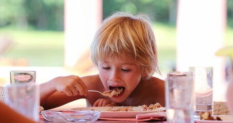 Candid young blond boy at lunch eating with family outside casual