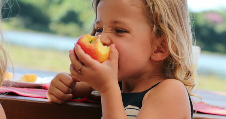 Child girl eating apple outside chewing