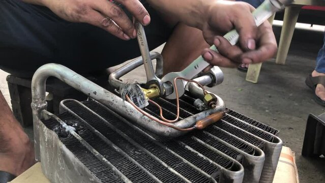 Technician is disassembling the heat exchanger evaporator component of a car on the street pavement. Close up