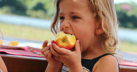 Child girl eating apple outside chewing