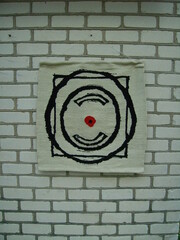 Woven tapestry black and white, square and circle composition, red dot in the middle, brick wall.