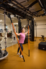 Adult smiling caucasian woman doing sport exercise with sports sticks in gym