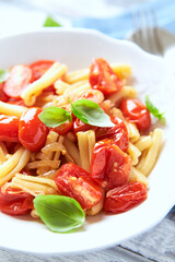 Casarecce pasta withe cherry tomatoes and fresh basil. Bright wooden background. Close up.