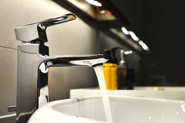 Close up shot of opened chrome faucet release the water into a ceramic basin in the luxury bathroom
