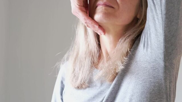 A woman with gray hair massages and pats her neck with sagging skin with her hands. Concept of loss of collagen and sagging skin in adulthood.