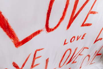 Multiple drawings of the word LOVE hand-painted in bright red forming a pattern on a plain white...