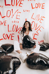 Woman sitting with kisses lipstick hold black foil balloons, the word LOVE hand-painted on plain...