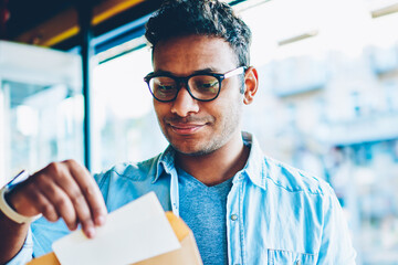 Cropped image of mature intelligent male person in trendy eyewear putting piece of paper inside...