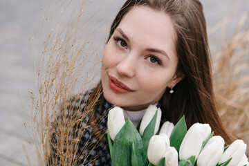 Young woman walking on the street with bouquet bunch of fresh spring tulips flowers, wind cold moody weather, celebrating International Women's Day. 8th of March holiday. Festive concept
