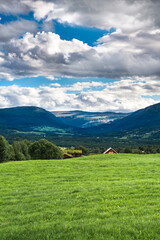 Lush grassland of Oppdal valley, in Trøndelag Norway with a farm tucked behind a rolling hill,...