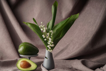 image of an avocado in a dish and a vase with flowers on a textured gray background
