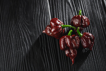 fresh brown extra hot carolina reaper chocolate pepper on black wooden rustic background