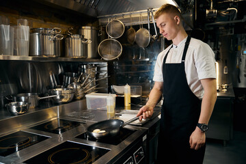 Side view of caucasian male chef frying sweet cheesecakes in pan on stove