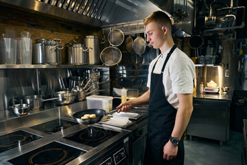 Side view of focused male chef frying sweet cheesecakes in pan on stove