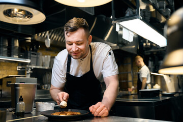 Smiling male chef adding cream in spoon to frying waffle on plate at table