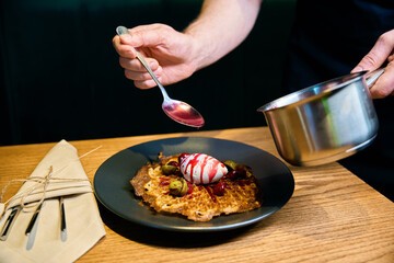 Partial male chef pouring jam to frying waffle with fruits on plate at table