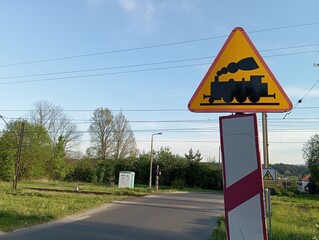 A railway crossing sign with a rural view in the background