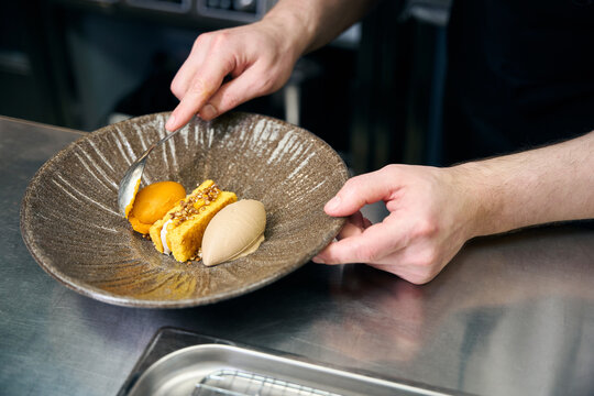 Partial chef adding chocolate cream to cookie in plate at table in restaurant