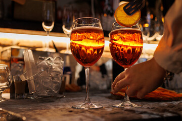 Bartender makes two glasses of cocktail Aperol spritz on bar counter, adds fresh orange slices....
