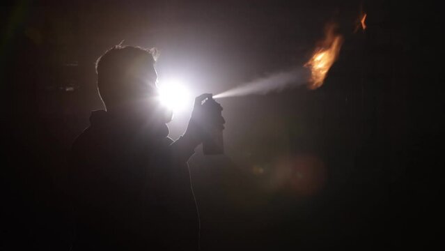Flame creativity, Flame artistry, Fire precautions. Shadowy figure in misty environment uses spray can to ignite striking fire burst, wearing gas mask for protection.