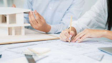 Professional engineer measures house model while skilled designer writes down in blueprint. Work...