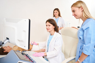 Obraz premium Gynecologist doing ultrasound scanning of woman pregnant belly near colleagues
