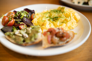 A nutritious brunch serving with fluffy scrambled eggs, a vibrant mixed salad, avocado toast, and seeds.