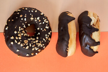 3 Chocolate covered doughnut with crush nuts on top on orange and beige background.