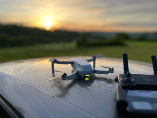 Kontroler drona z wyświetlaczem i dron w tle w plenerze ze wschodem słońca © VILKTERIO