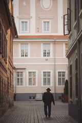 Man walking down an old street, view from the back. Rear view of a stylish man in a hat and coat walking down the street.