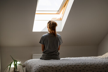 Rear view lonely woman depressed sits on alone on bed at home. Mental illness, anxiety, worries.
