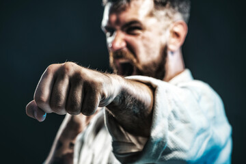 Karate fighter practicing punch in gym. Selective focus on fist. Strength and motivation. Screaming man in kimono ready for karate training. Angry karate man in fighting position. Mixed martial art.